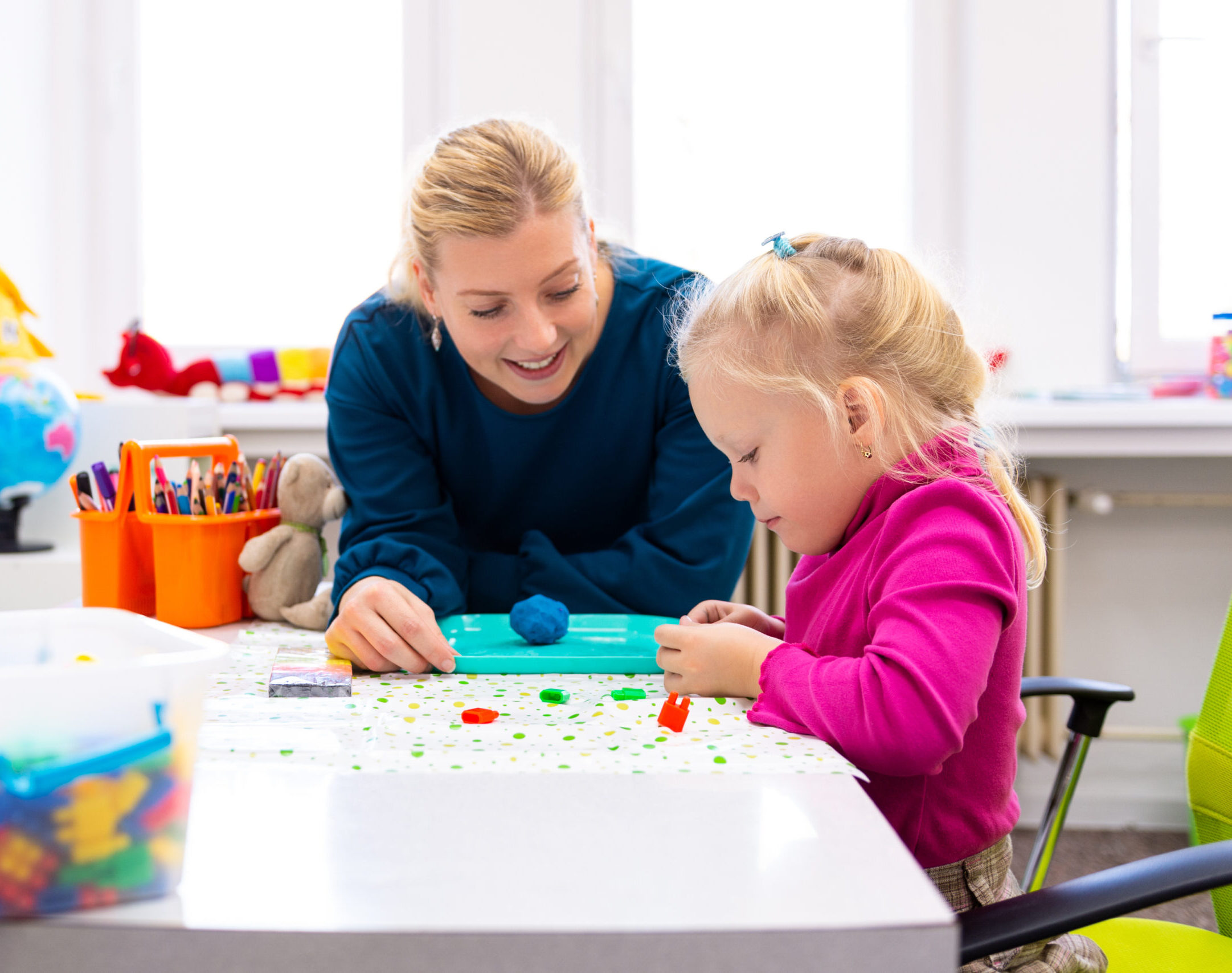 Toddler girl in child occupational therapy session doing sensory playful exercises with her therapist.