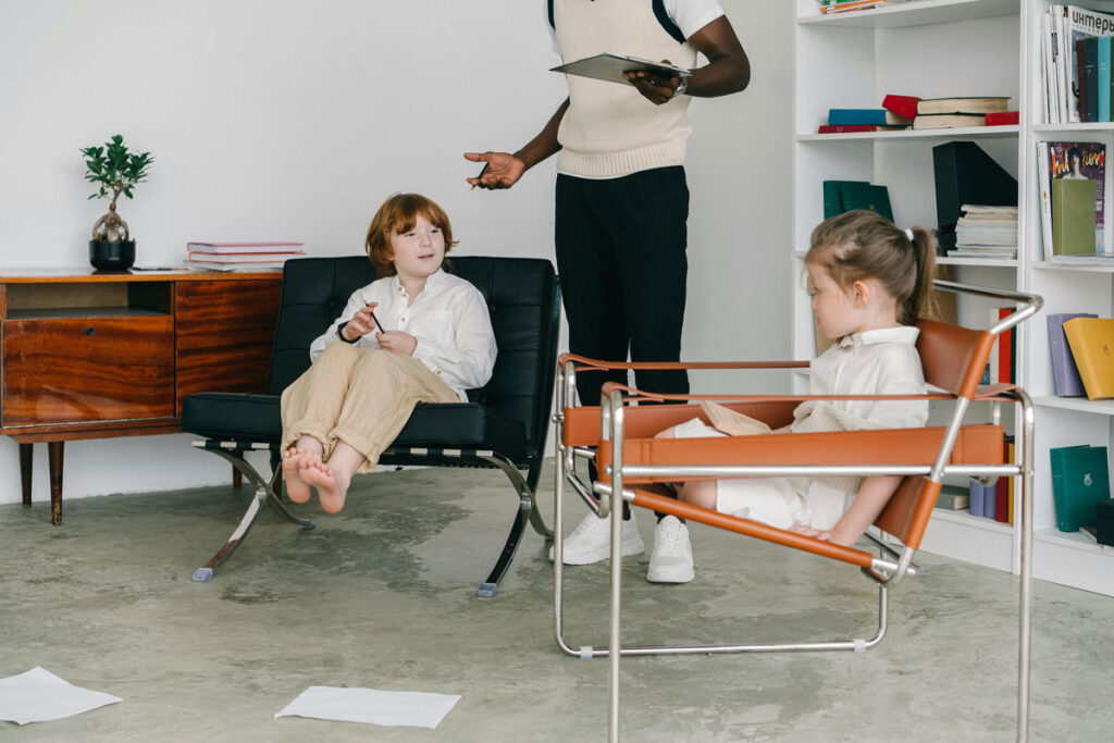 Two children sitting in armchairs while getting taught by an adult