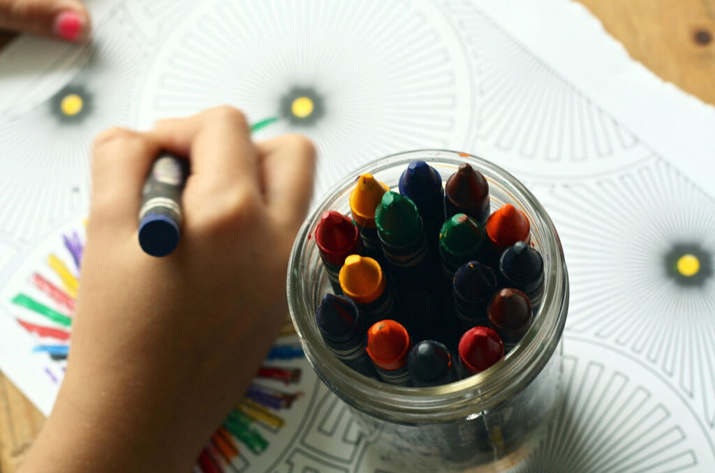 Zoomed in picture of a childs hand while they use crayons to colour in 